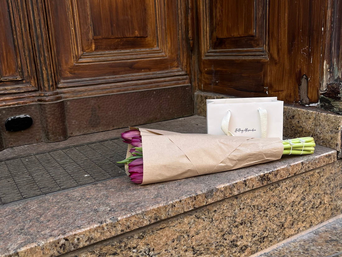 A bouquet of tulips resting beautifully on steps of someone's front porch next to a Hillary Alexandria shopping bag. 